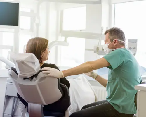 Dentist in green scrubs talking with a patient seated in the dental chair
