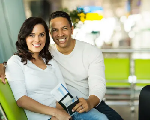 Smiling couple sitting together at an airport holding travel documents