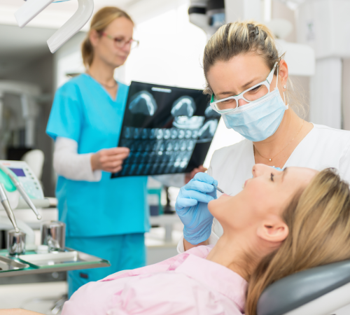 Dentist examining a patient while an assistant reviews dental X-rays